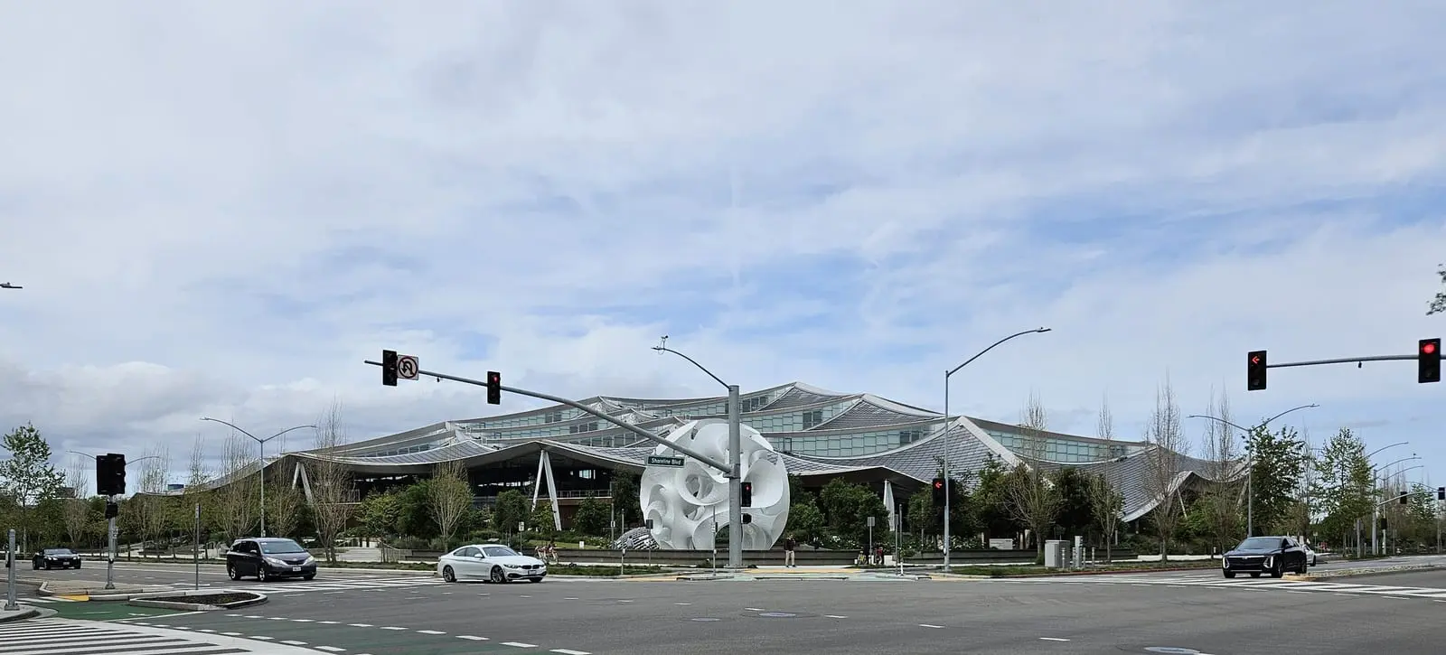 Google's Gradient Canopy building in Mountain View, with its curved tent-like roof panels, seen across a road junction with traffic lights.