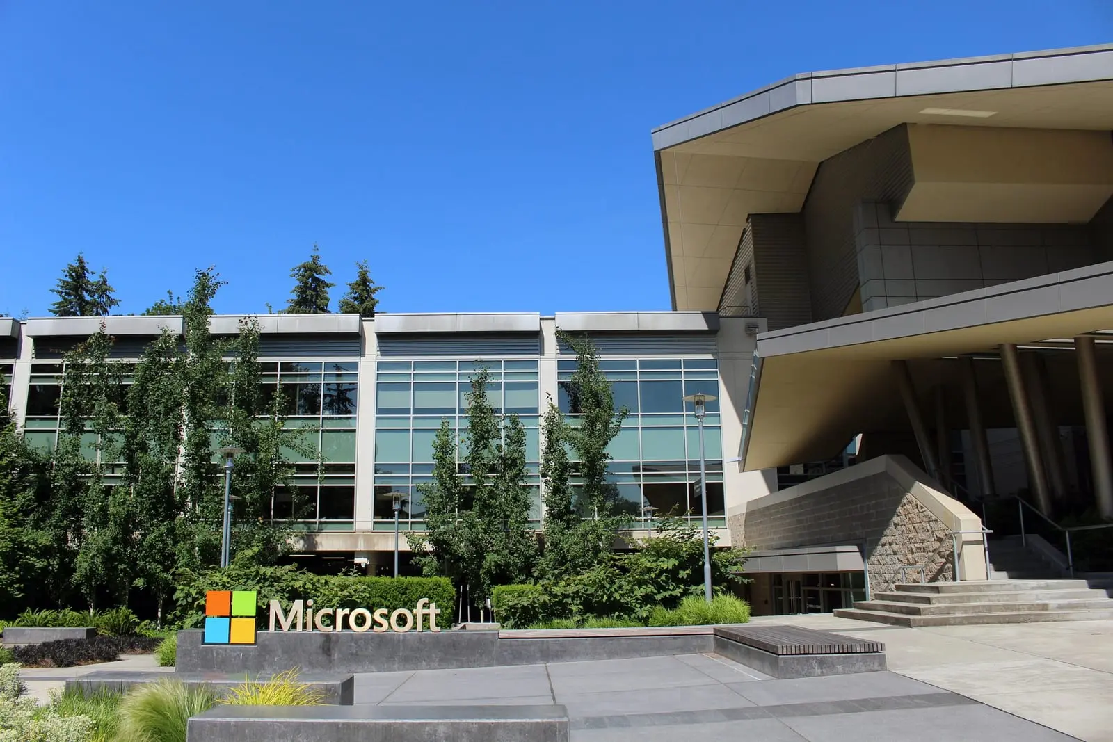 Building 92 on Microsoft's headquarters campus in Redmond, Washington, with a Microsoft logo sign in front of glass office buildings under a blue sky.