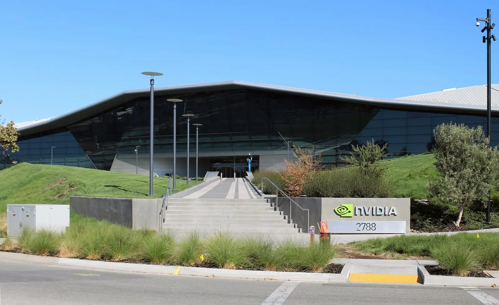 The angular glass front of NVIDIA's headquarters in Santa Clara, California, with a wide stairway and an NVIDIA sign in front.
